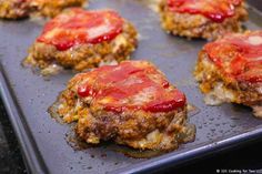 some meat patties with ketchup are on a baking sheet