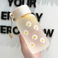 a hand holding a white and yellow water bottle with daisies on the side that says your energy grow