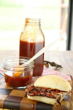 a sandwich sitting on top of a wooden cutting board next to jars of ketchup