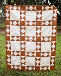 a brown and white quilt hanging from a line in the grass with trees in the background