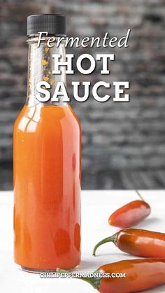 an orange hot sauce in a glass bottle next to some chili peppers