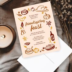 a pink and gold thanksgiving feast card on top of a white envelope with a candle