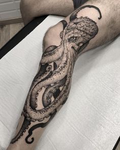 an octopus tattoo on the leg of a man in black and grey ink, sitting on a bed