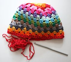 a multicolored crocheted beanie sits next to a knitting needle