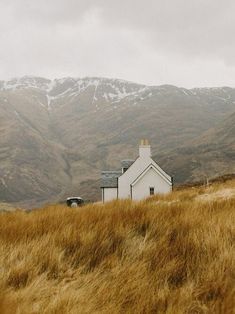 a white house sitting on top of a lush green hillside next to a tall grass covered hill