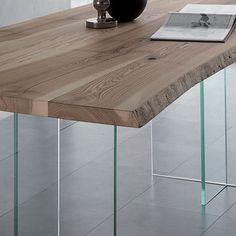 a wooden table with glass legs and a vase on it's end, in front of a white wall