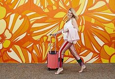 a woman is walking with her luggage in front of an orange and yellow flowered wall