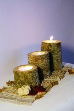 three candles are sitting on a table with some fabric around it and one candle is lit