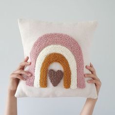 someone holding up a pillow with a heart in the middle and a rainbow on it