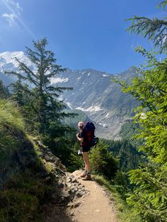 a person hiking up a trail in the mountains with trees on both sides and snow - capped peaks behind them