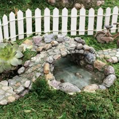 a miniature garden with rocks and plants in the grass next to a white picket fence