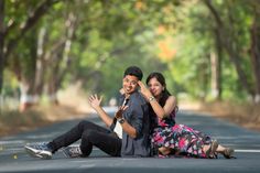 a man and woman sitting on the road with their arms around each other as they pose for a photo