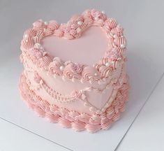 a heart shaped cake with pink frosting and decorations on it's sides, sitting on a white surface