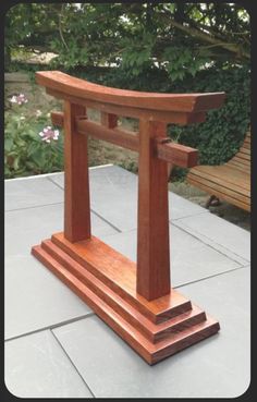 a small wooden object sitting on top of a cement floor next to a tree and bushes