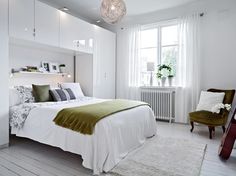 a bedroom with white walls and wood flooring has a green blanket on the bed