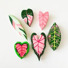 four decorated cookies in the shape of hearts and leaves on a white surface with green, pink, and red leaf shapes