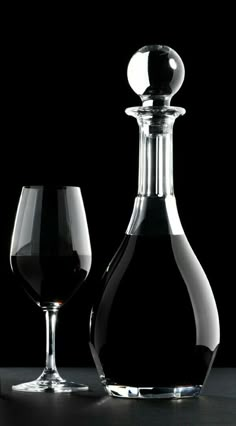 a decanter and wine glass sitting on a table next to each other in front of a black background