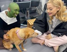 two people sitting on the floor petting a dog with a green man in the background