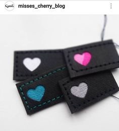 two black and one pink heart tags with green stitching