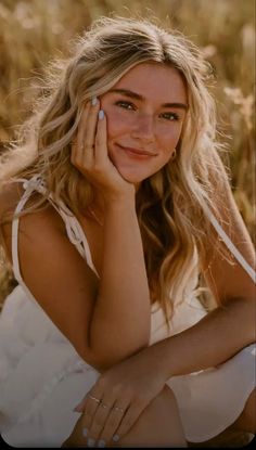 a woman sitting in a field with her hand on her face and looking at the camera