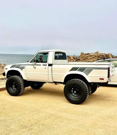 a white pickup truck parked on top of a sandy beach next to the ocean and rocks