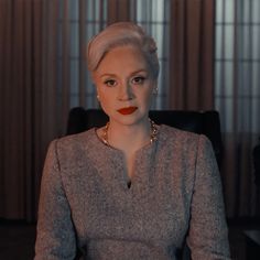 a woman sitting in a chair with red lipstick on her face and wearing a gray sweater