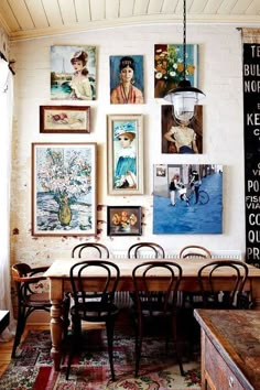 a dining room table with chairs and pictures on the wall above it, along with other art