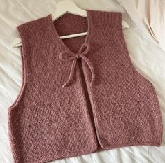 a pink sweater vest with a bow at the neck on a white bedding sheet