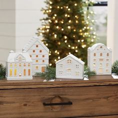 small white houses are sitting on a chest of drawers in front of a christmas tree