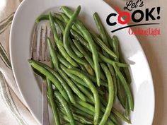 a white plate topped with green beans on top of a table next to a fork