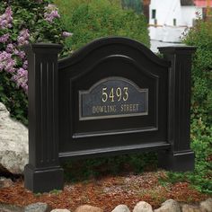 a sign that is in front of some rocks and bushes with purple flowers behind it