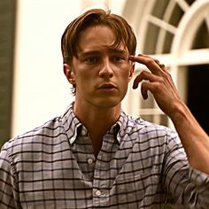 a young man is holding his hand to his ear and looking at the camera while standing in front of a house