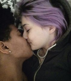 a woman and child kissing each other while laying on top of a bed with purple hair