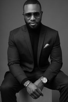 a man in a suit and sunglasses sitting on a stool