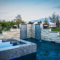 an outdoor swimming pool surrounded by stone walls and water features in the middle of it