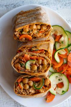 a white plate topped with two wraps filled with meat and veggies next to sliced cucumbers