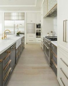 a large kitchen with white cabinets and gold handles on the countertops, along with stainless steel appliances