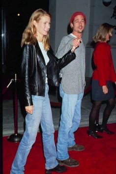 a man and woman standing on a red carpet pointing at something in front of them