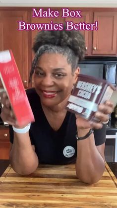 a woman sitting at a kitchen table holding up a box of brownies with the words make box brownies better