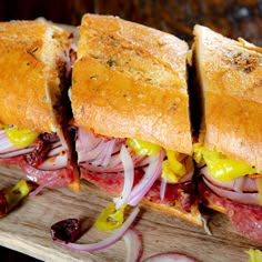 two sandwiches cut in half sitting on top of a cutting board with onions and meat