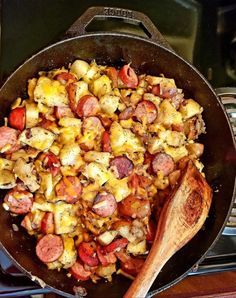 a skillet filled with sausage and potatoes on top of a stove next to a wooden spoon