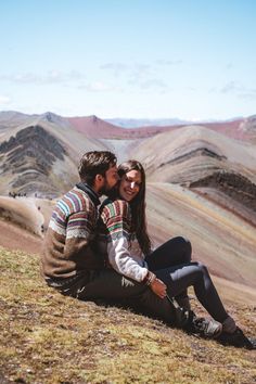 a man and woman sitting on top of a hill