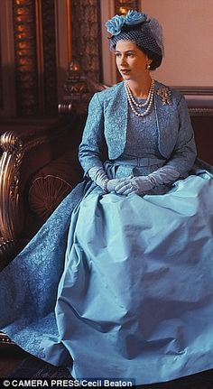 the queen of england is sitting on a couch wearing a blue dress and matching hat