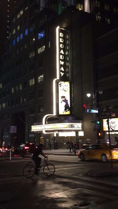 a man riding a bike down a street next to a tall building with a neon sign on it