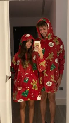 a man and woman in matching christmas pajamas taking a selfie with their cell phone