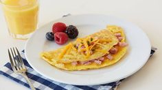 an omelet with ham, cheese and berries on a plate next to a glass of orange juice