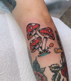 a person with a tattoo on their arm that has red mushrooms and flowers all over it