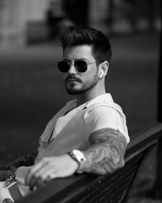 a man with tattoos sitting on a park bench wearing sunglasses and looking off to the side