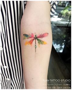 a colorful dragonfly tattoo on the arm