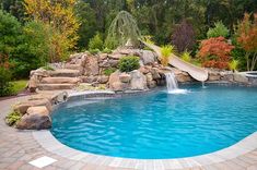 a pool with a slide in the middle of it and rocks on both sides, surrounded by trees